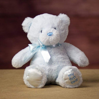 A beige sitting bear with the words "My First Teddy" sewn onto the feet