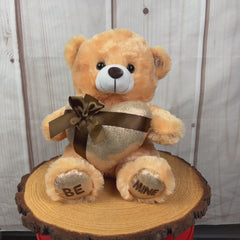 A beige bear that is 11 inches tall while sitting holding a shiny gold gift-wrapped heart with BE MINE embroidered on its feet