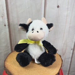 A black and white cow that is 7 inches tall while sitting wearing a yellow bow