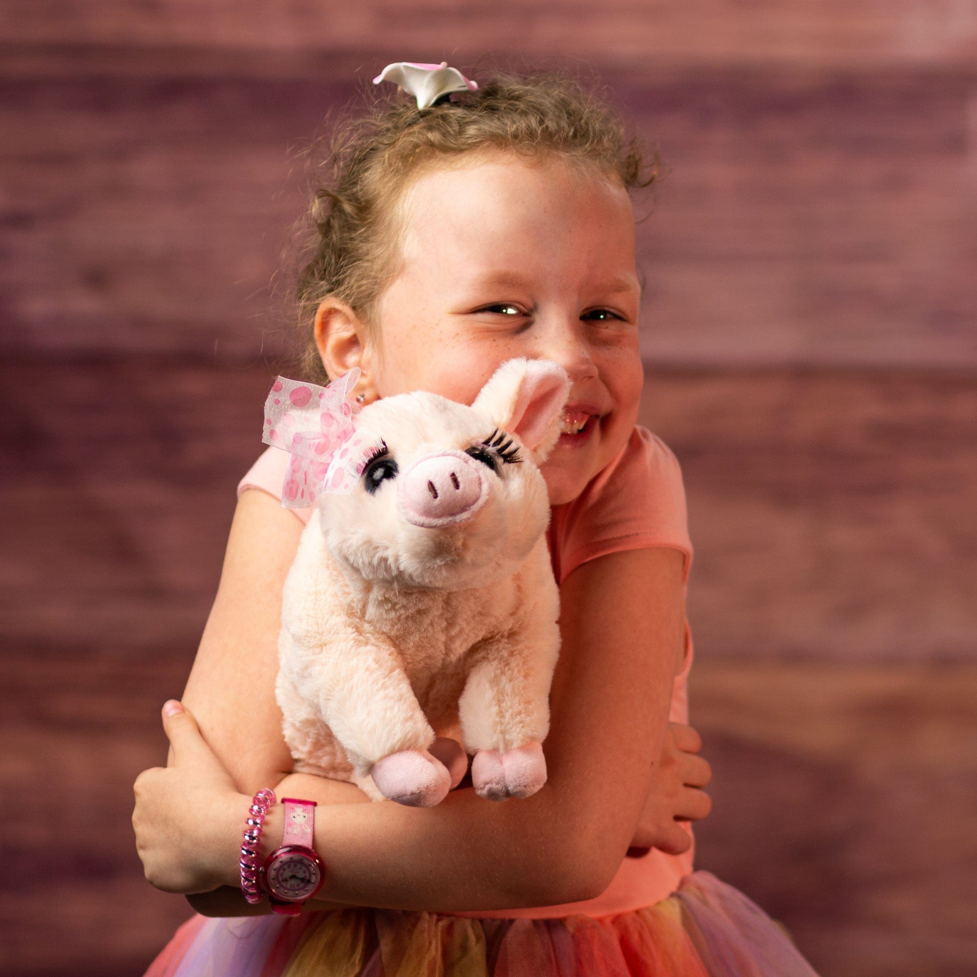 girl holding 12 in stuffed pink pig wearing a bow and has eyelashes