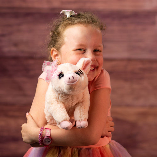 girl holding 12 in stuffed pink pig wearing a bow and has eyelashes