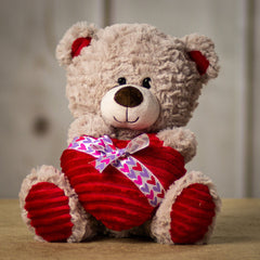 A beige bear that is 10 inches tall while sitting holding a plush heart wrapped in a Valentine bow tie