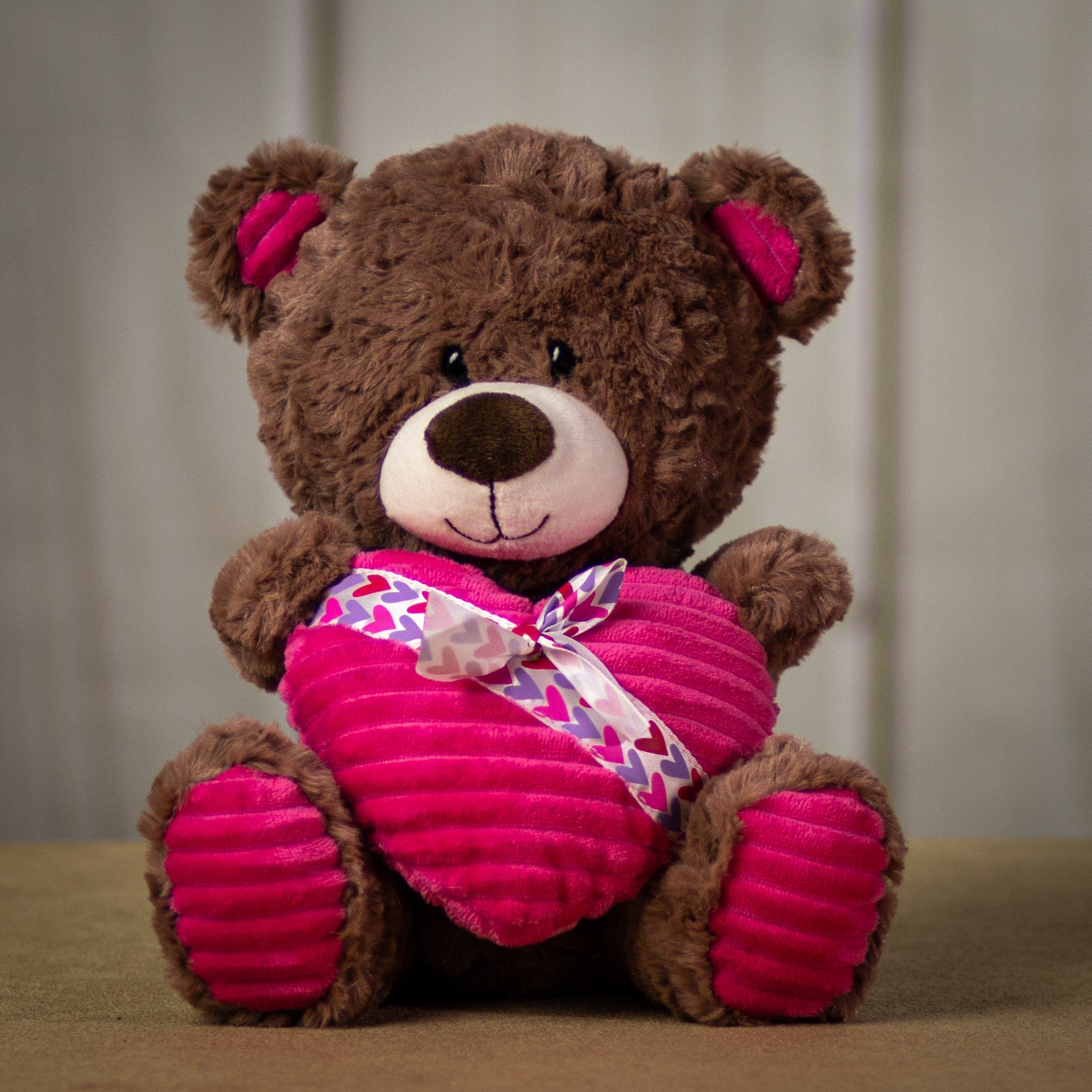 A brown bear that is 10 inches tall while sitting holding a plush heart wrapped in a Valentine bow tie