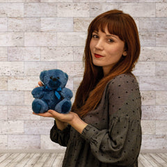 A woman holds a blue bear that is 6 inches tall while sitting