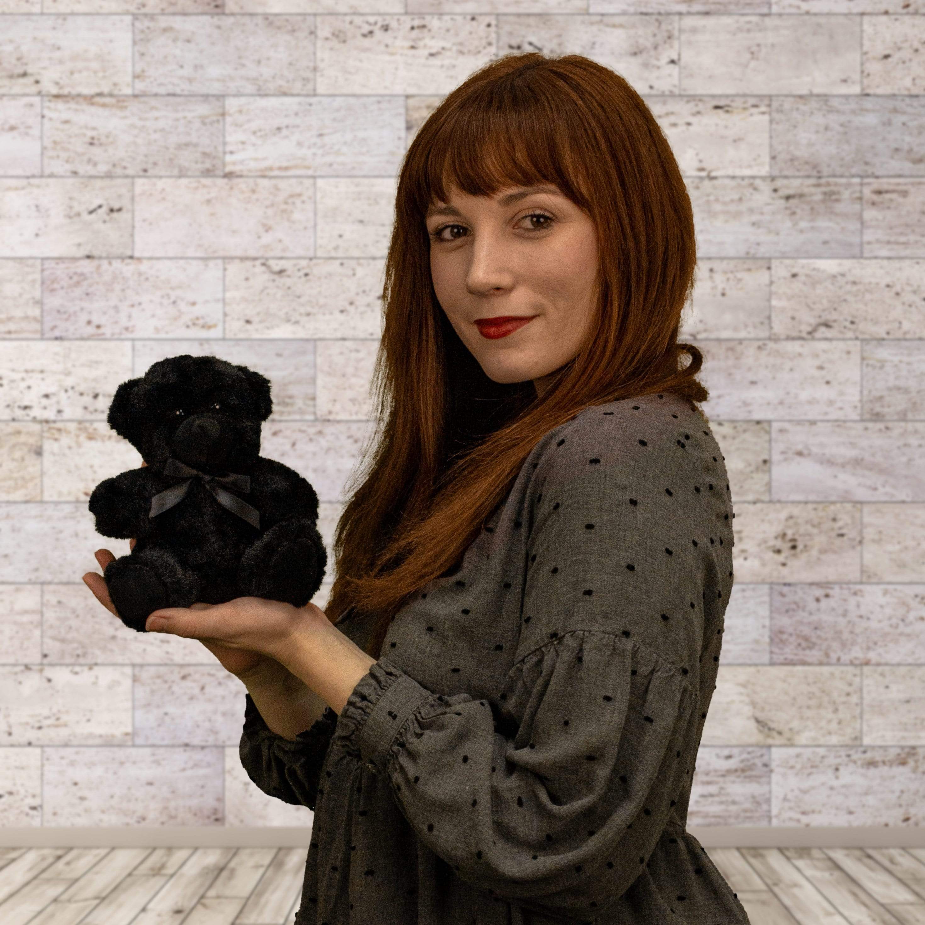 A woman holds a black bear that is 6 inches tall while sitting