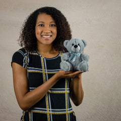 A woman holding a gray bear that is 6 inches tall while sitting