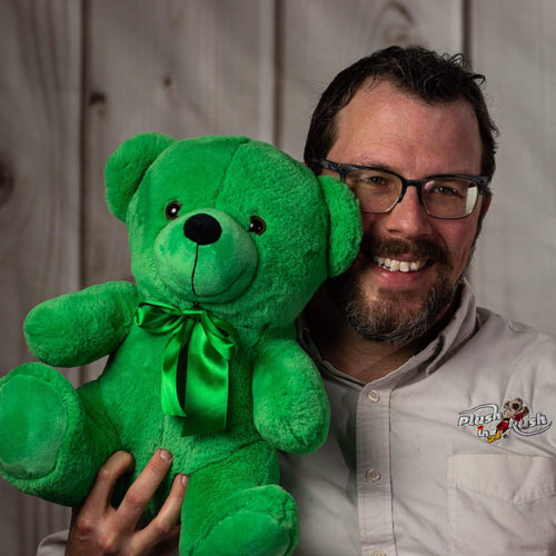 A man holds a green bear that's 14 inches tall while sitting