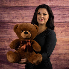 A woman holds a brown bear that is 14 inches tall while sitting wearing a matching bow