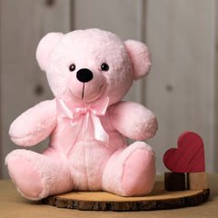 A light pink bear that is 14 inches tall while sitting wearing a matching bow next to wooden blocks