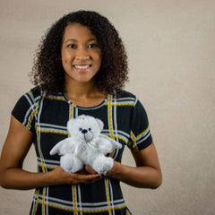 A woman holds a white bear that is 6 inches tall while sitting wearing a pair of wings and a silver halo.