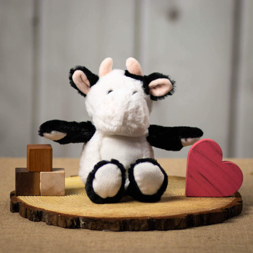 A black and white cow that is 11 inches tall while standing sitting on top of a piece of wood