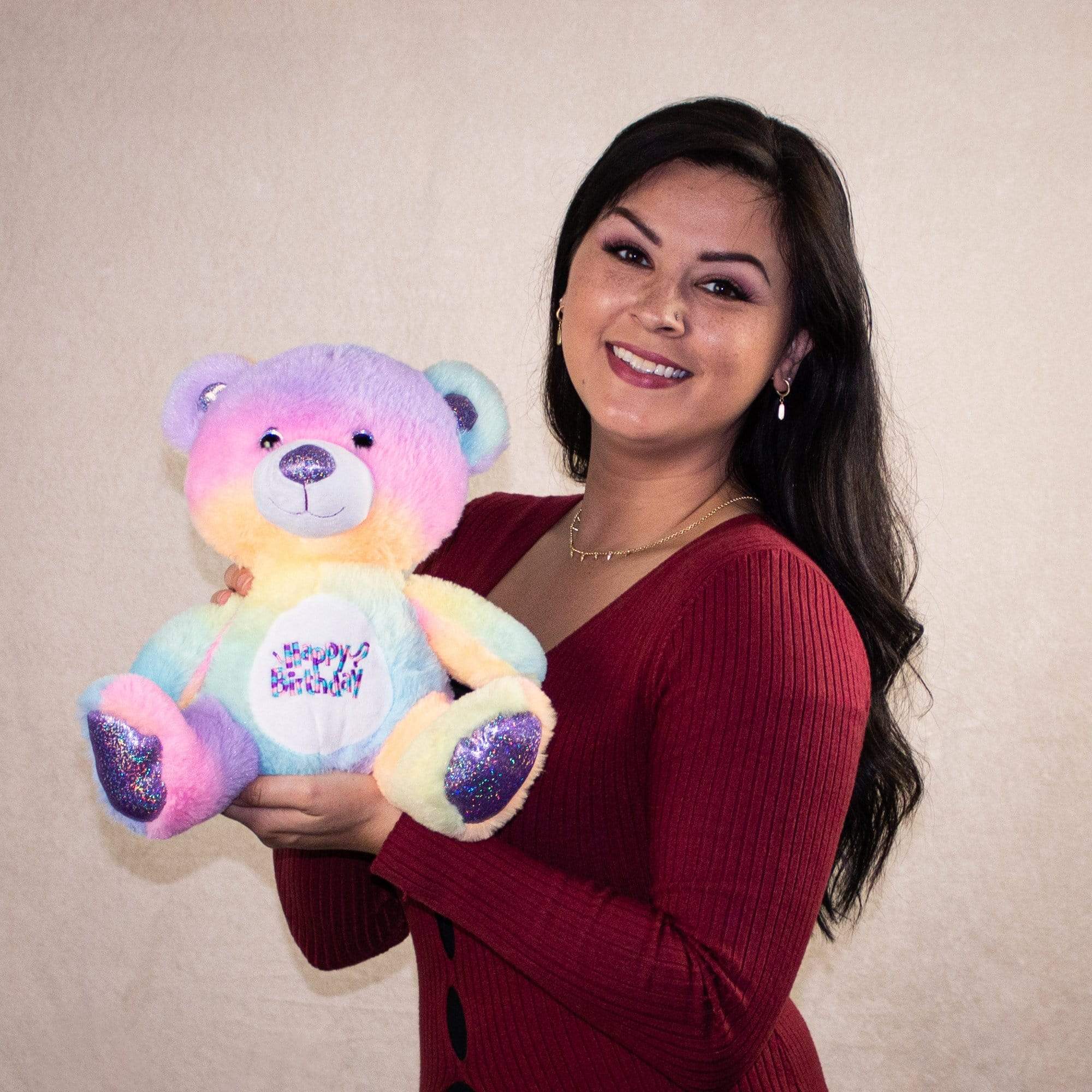 An adult woman holds a colorful teddy bear that says Happy Birthday on its stomach