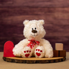 A nice looking cream valentine bear sitting on a piece of wood