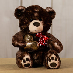 A brown bear that is 17 inches tall with paw prints on its feet wearing a red heart covered bow holding a shiny, gold heart