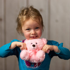 A little girl holding a pink bear that is 6 inches tall while sitting wearing a matching bow