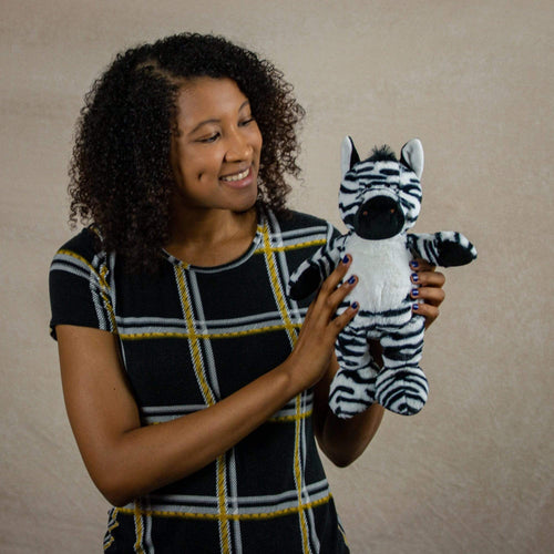 A woman holds a black and white stripped zebra that is 13 inches tall while standing