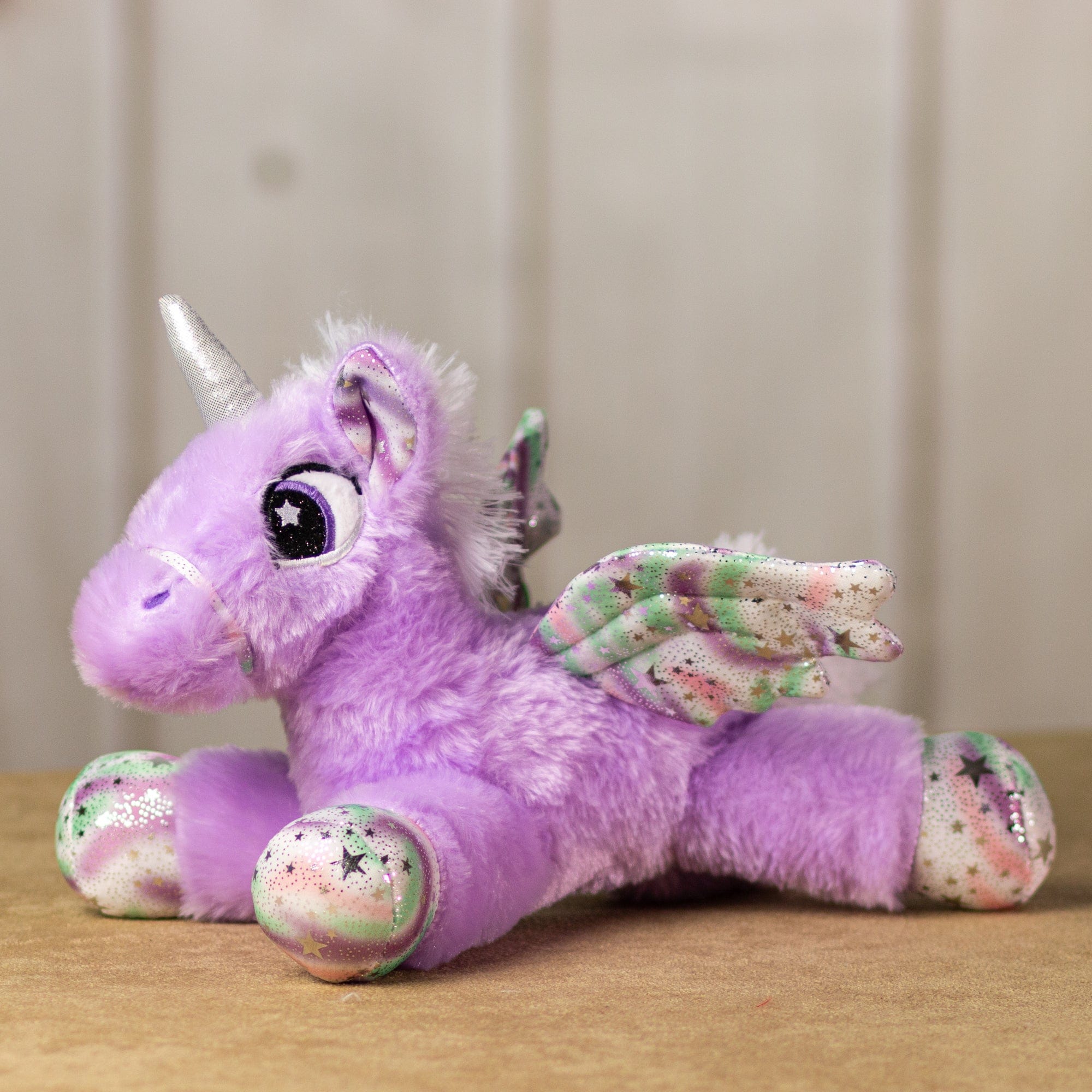 A purple unicorn that is 14 inches while laying down with embroidered eyes, shiny paws, wings and horn.