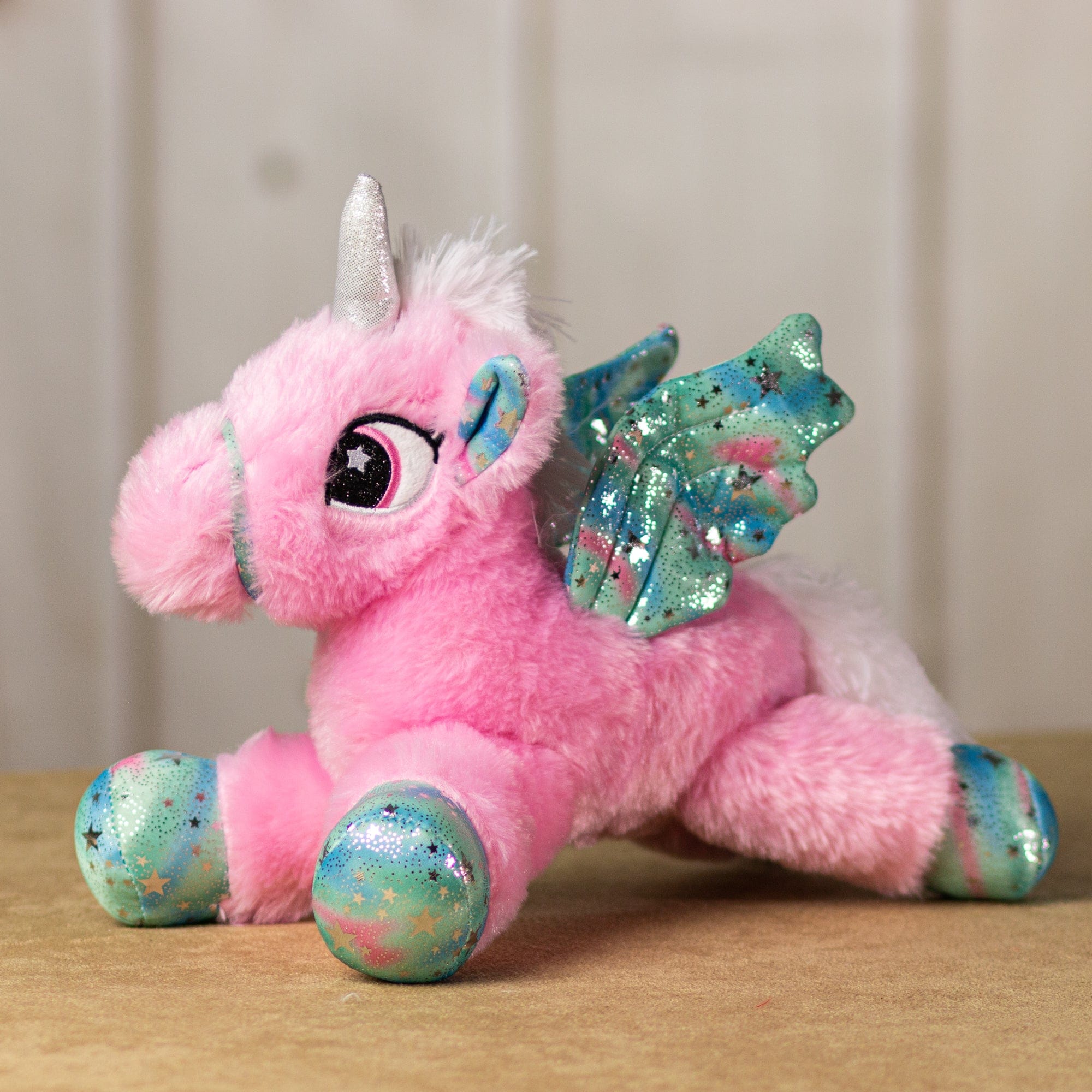 A pink unicorn that is 14 inches while laying down with embroidered eyes, shiny paws, wings and horn.