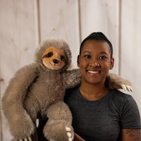 A woman holding a fuzzy, brown sloth that is 20 inches tall while standing