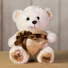 A white bear that is 11 inches tall while sitting holding a shiny gold gift-wrapped heart with BE MINE embroidered on its feet