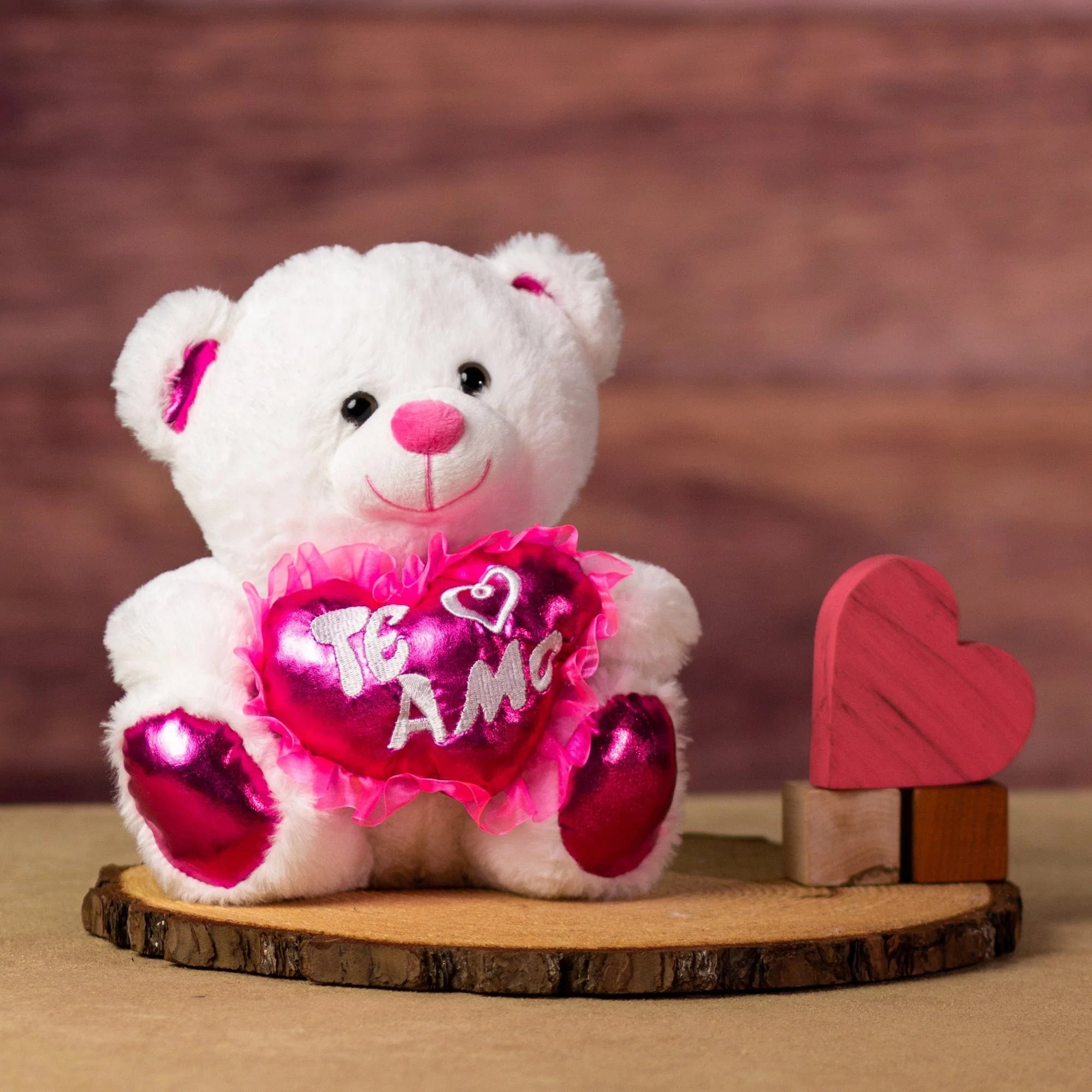 A white bear that is 10 inches tall while sitting with pink feet and ears holding a shiny pink "Te Amo" heart next to wooden blocks