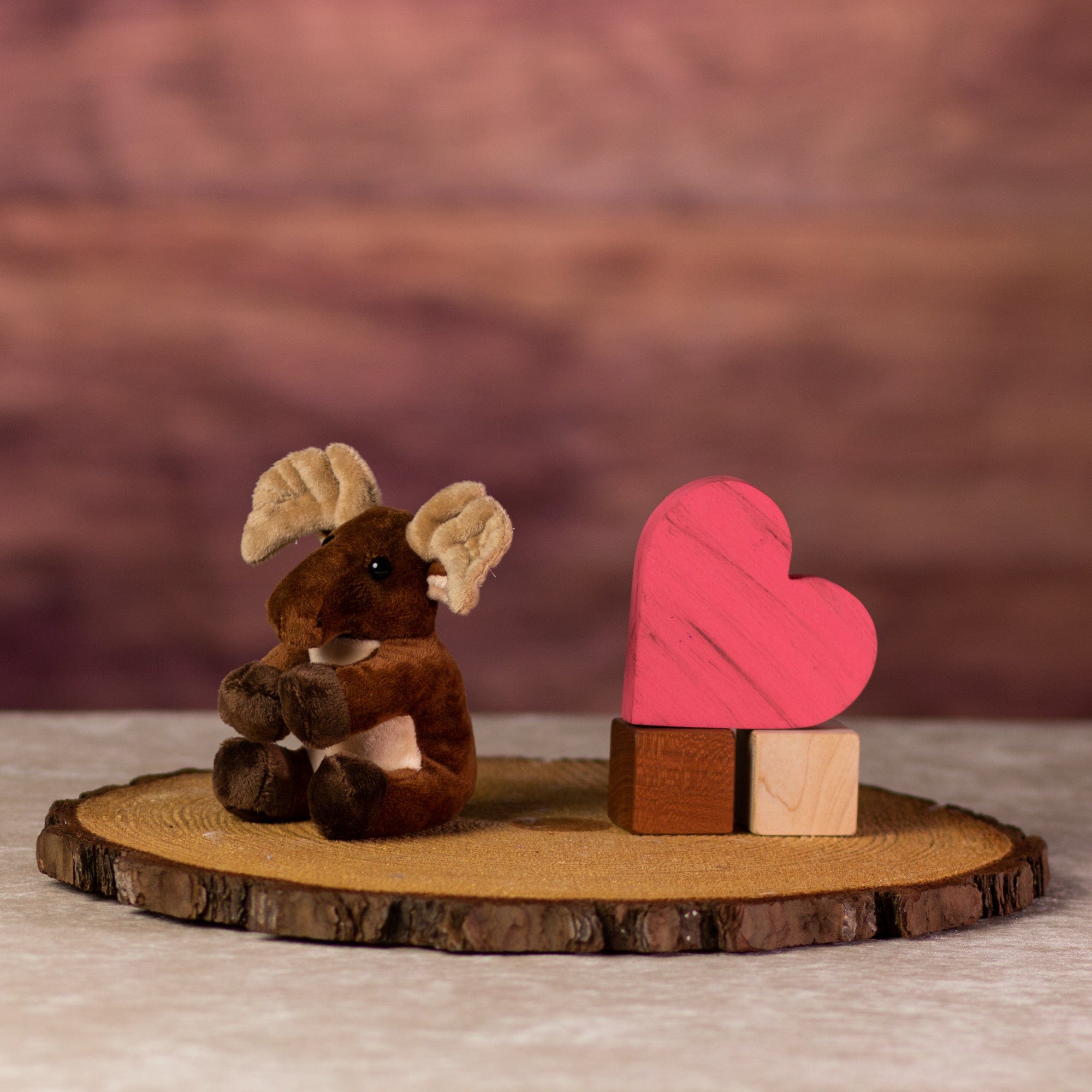 A brown moose that is 5 inches tall while sitting on top of a piece of wood