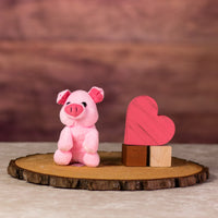 A sitting pink pig that is 5 inches tall next to wooden blocks