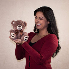 A woman holding a brown bear that is 7 inches tall while sitting with paw prints on its feet