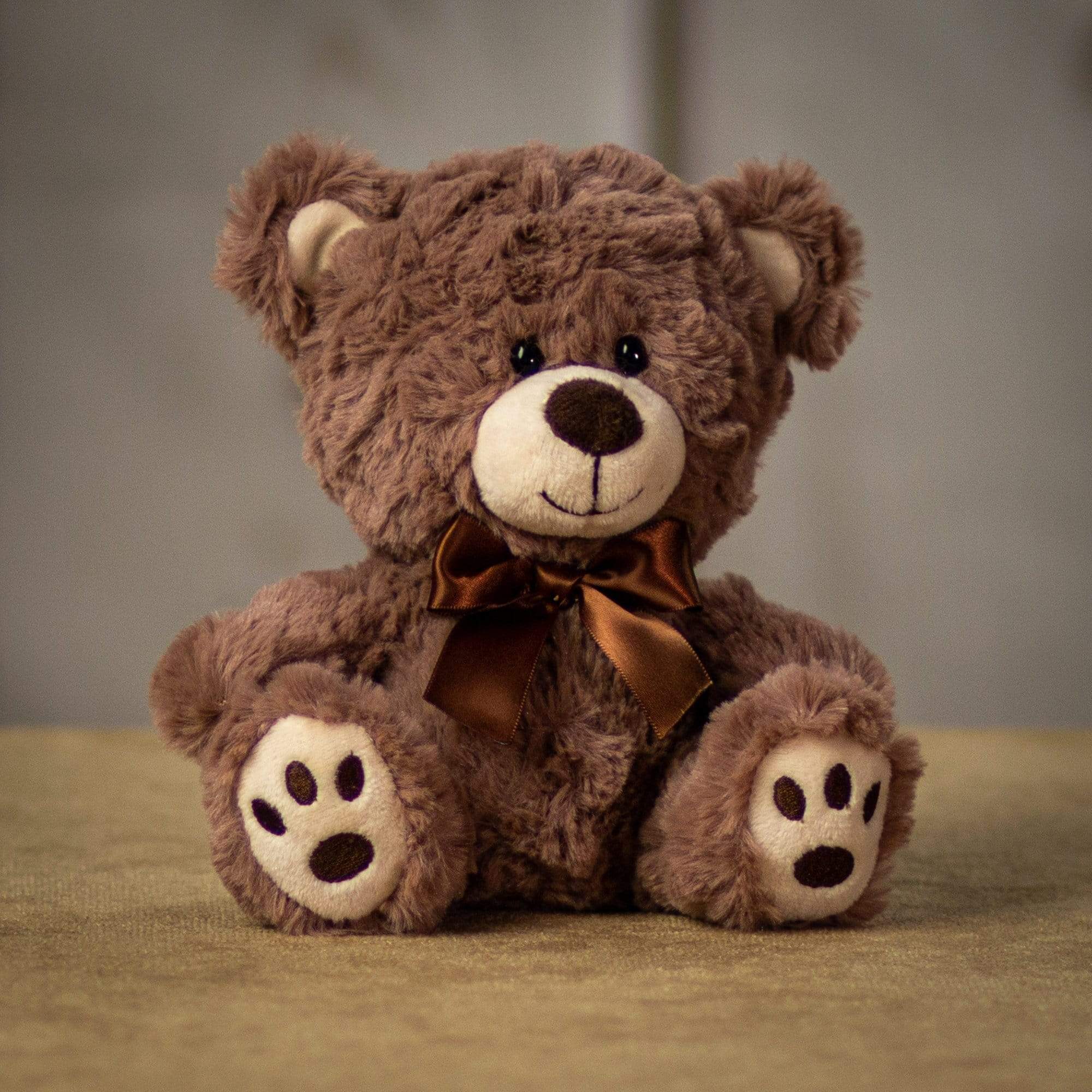 A brown bear that is 7 inches tall while sitting with paw prints on its feet