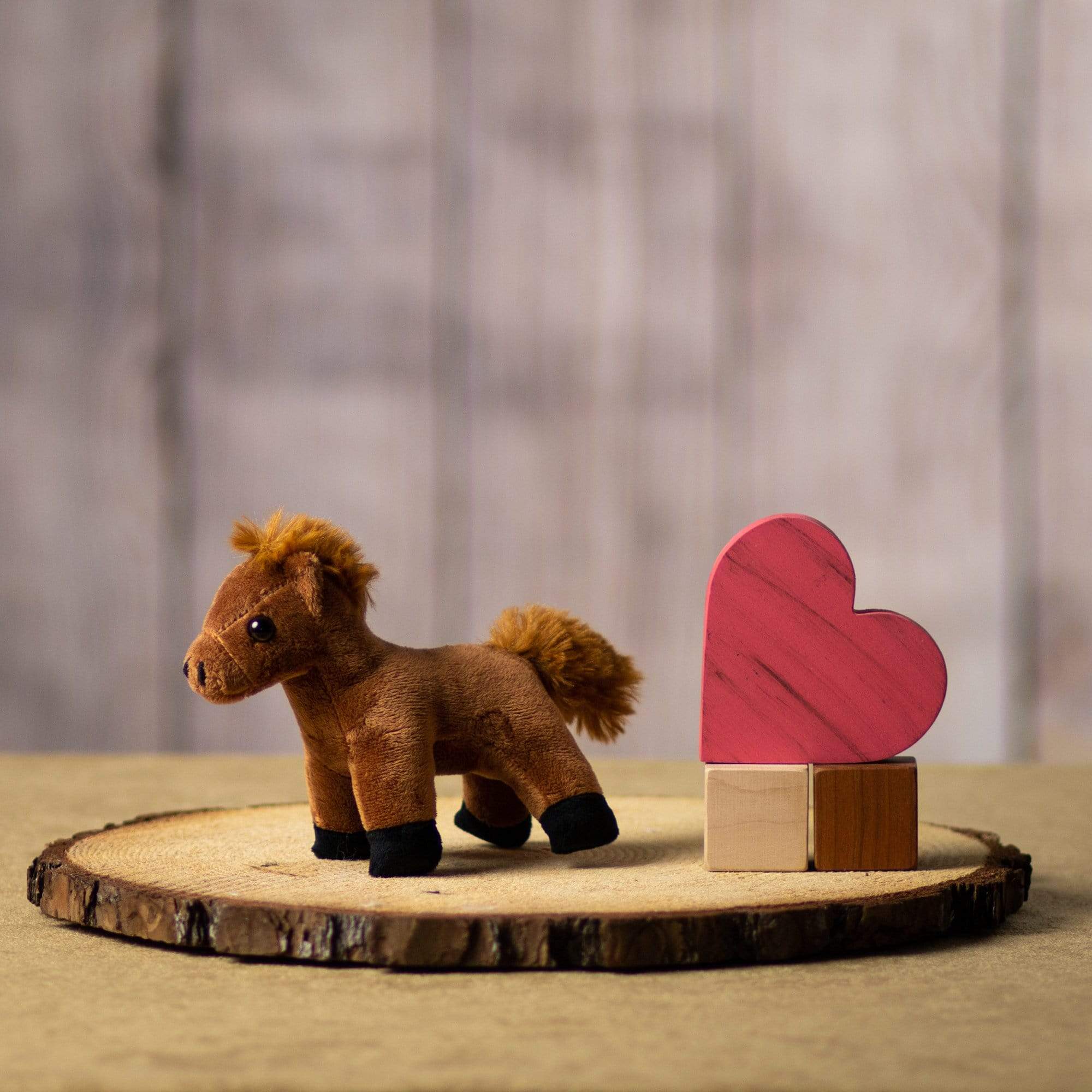 A small brown horse stuffed animal sitting on a log slice with props