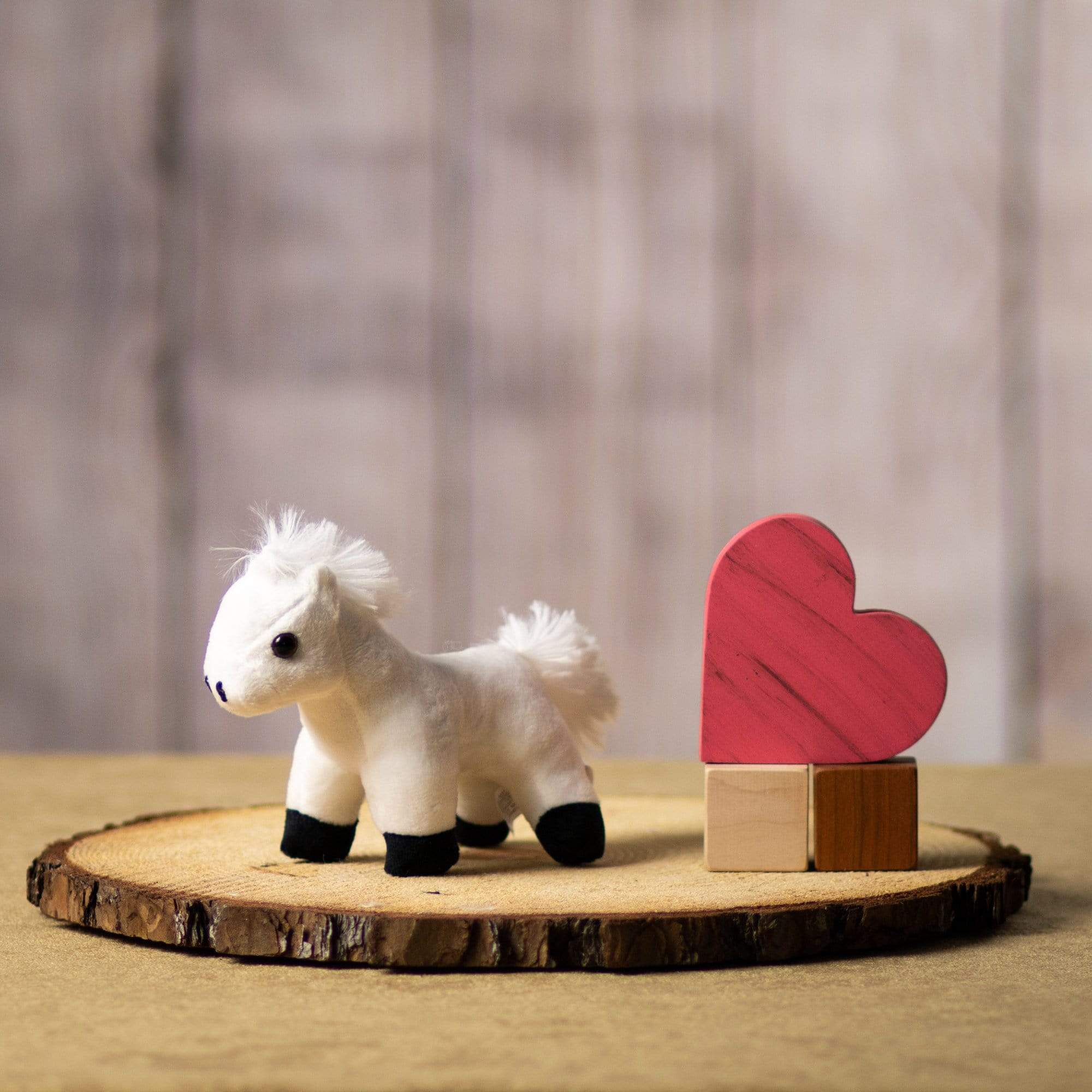 A small white horse stuffed animal sits on a log slice with props