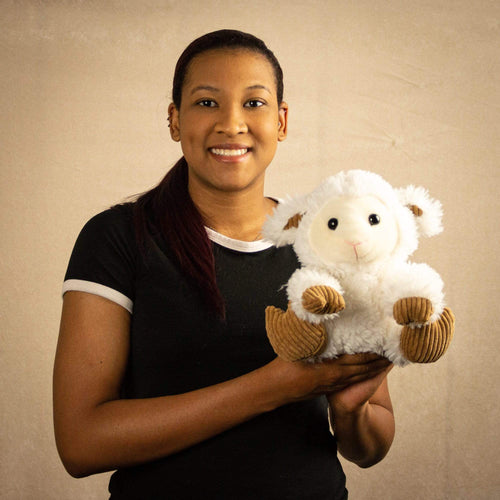 A woman holds a scruffy white lamb that is 9.5 inches tall while sitting with brown hooves