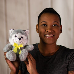 A woman holding a gray husky that is 7 inches tall while sitting wearing a yellow bow