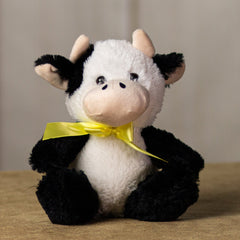 A black and white cow that is 7 inches tall while sitting wearing a yellow bow