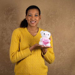 A woman holds a white bear that are 6 inches tall while sitting holding a pink heart that says "Happy Mother's Day""