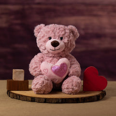 A pink bear that is 10 inches tail while sitting holding a heart accented with smaller shiny hearts next to wooden blocks