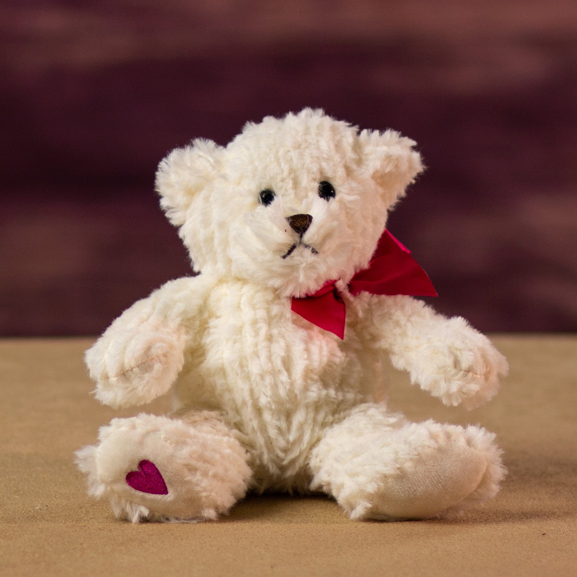 A cream bear that is 7 inches tall while sitting with a heart at the bottom of its foot