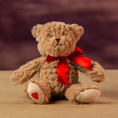 A beige bear that is 7 inches tall while sitting with a heart at the bottom of its foot