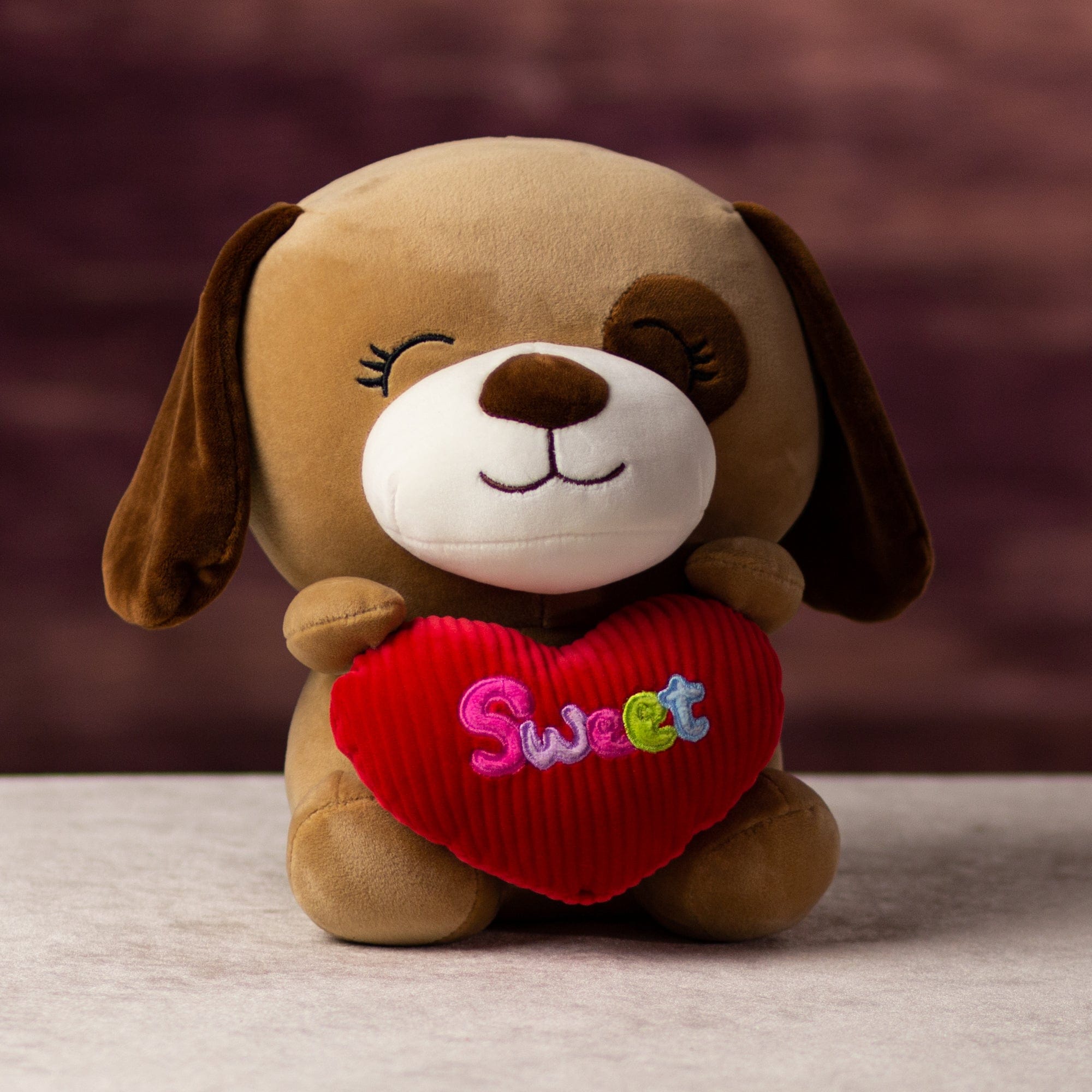 A brown dog that is 10.5 inches tall while sitting holding valentine heart