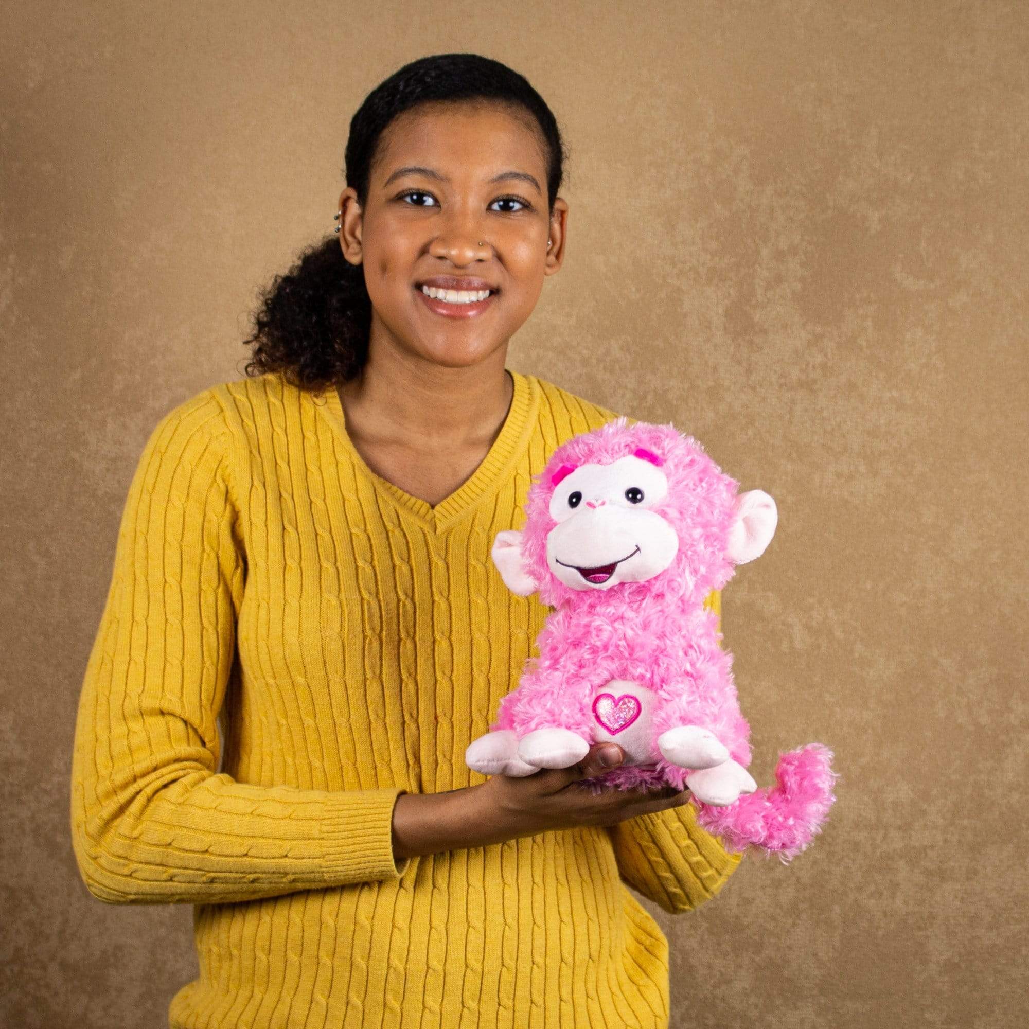 A woman holds a pink singing/animated monkey that is 10 inches tall while sitting